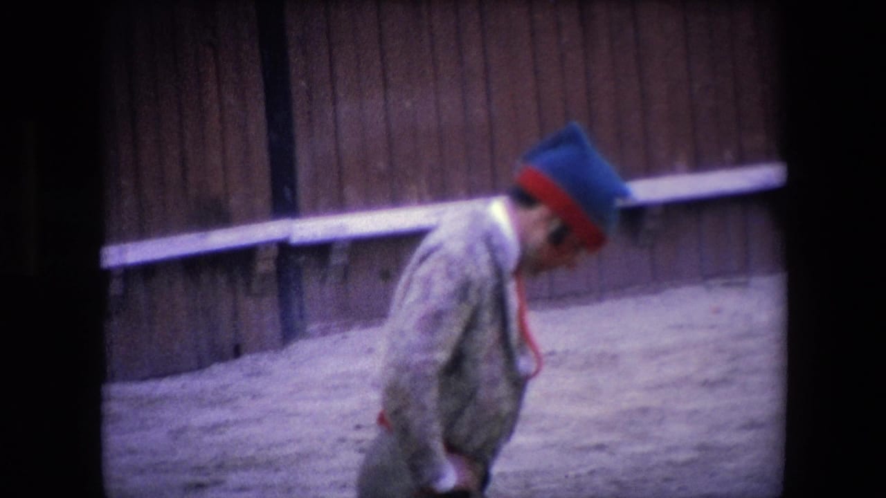 In 1971 Barcelona footage, a matador in a patterned suit and blue-red hat moves across the sandy arena in front of wooden bullring barriers.
