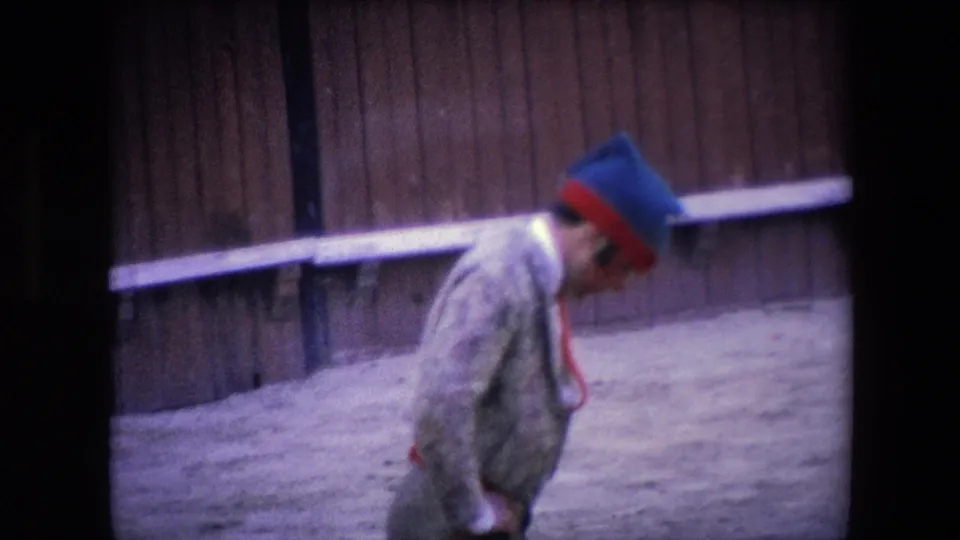 In 1971 Barcelona footage, a matador in a patterned suit and blue-red hat moves across the sandy arena in front of wooden bullring barriers.