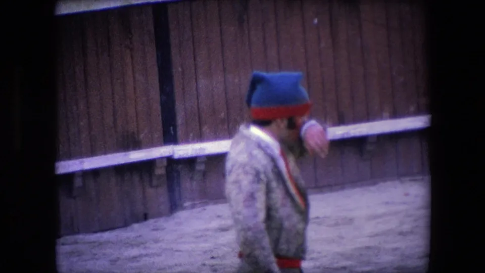 In the supplied 1971 Barcelona bullfighting clip, the matador stands in profile on the sandy arena floor with wooden barriers behind him.