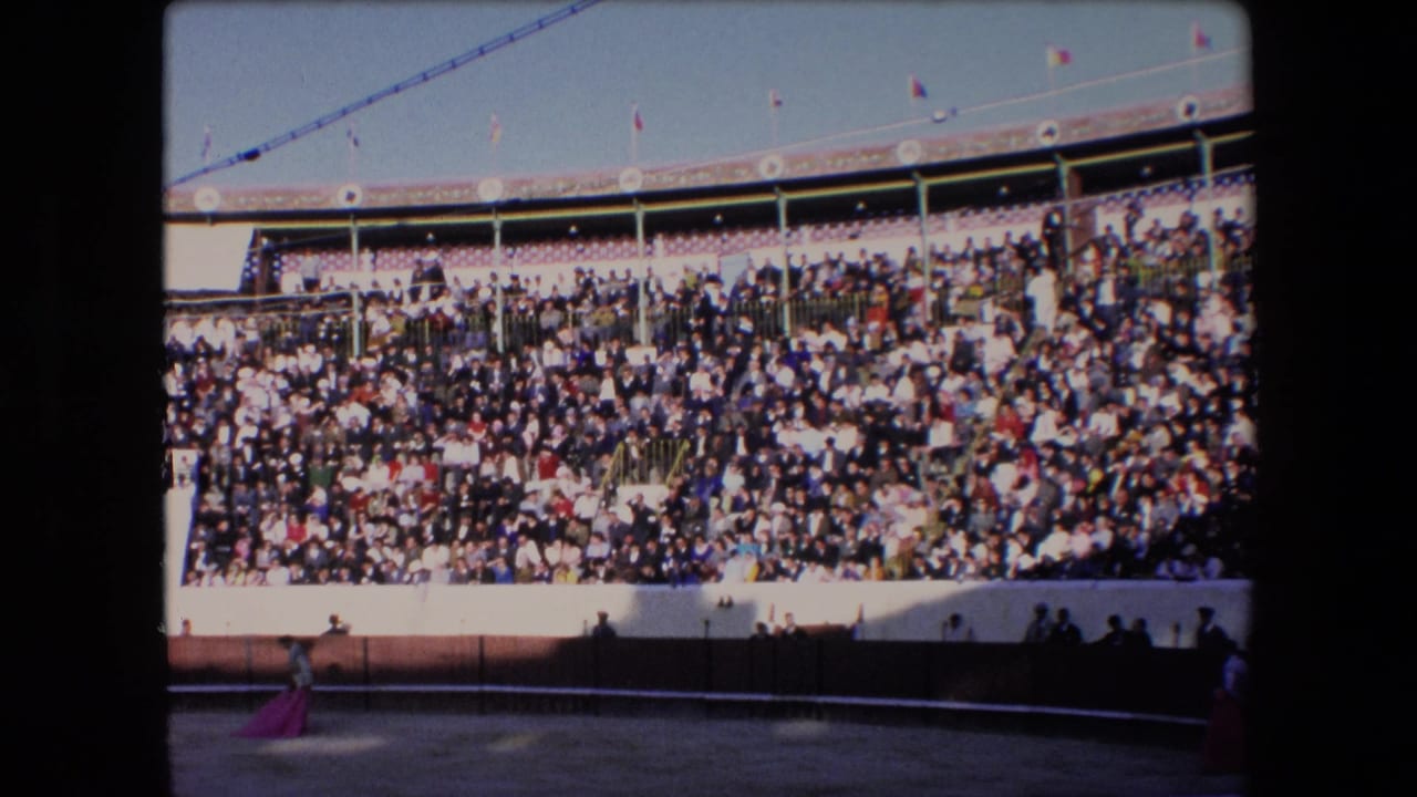 Wide view of a crowded bullring with a matador crossing the sandy arena.