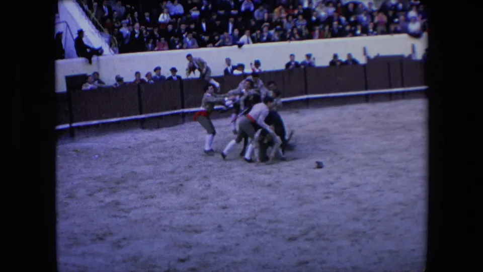 Men in light bullring clothing cluster around the bull on the sandy floor, with spectators visible above the barrier in the 1971 Barcelona arena.