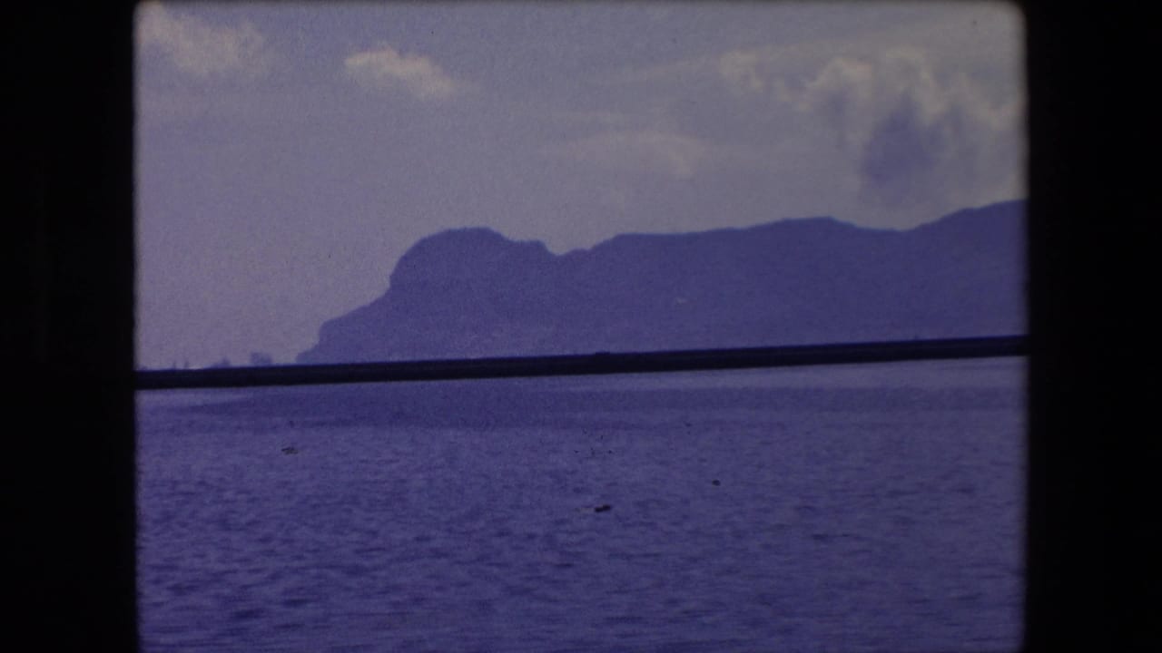 1971 Barcelona-area seascape with open water in the foreground, a dark mid-frame rail or window bar, and hazy mountains along the horizon.