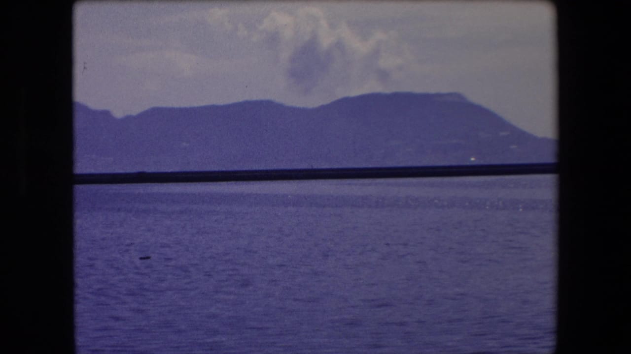Mountain and water view with clouds above, divided by dark window-like bars.