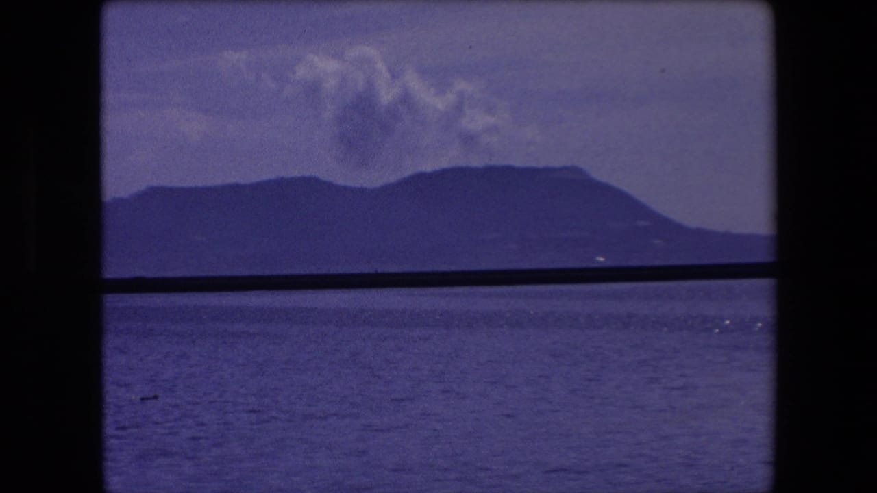 Blue sea and distant mountains under clouds with a dark horizontal edge in front.