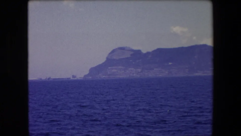 A later frame shows a different rocky coastal mountain or headland across dark blue water, with hazy sky and soft 8mm color shift.