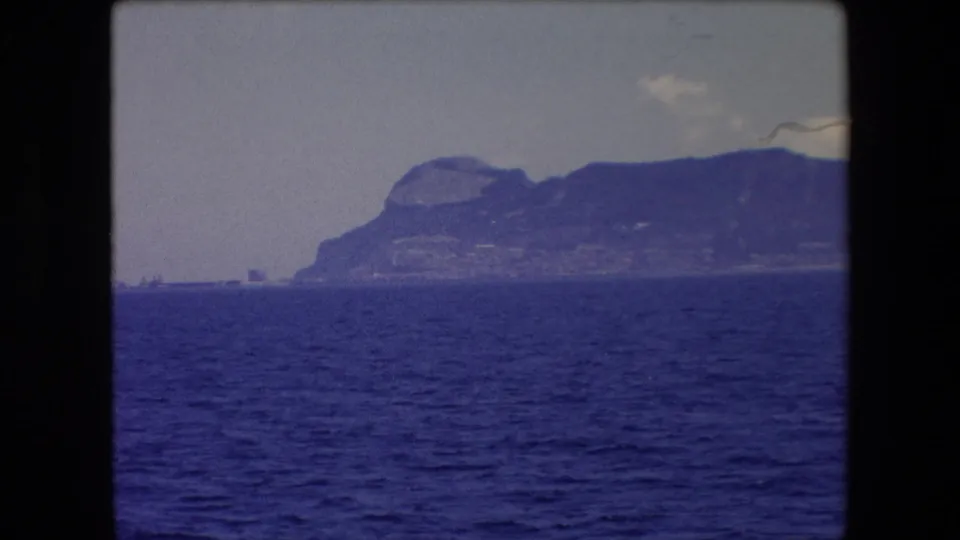 The 8mm frame holds on rippled blue sea, a far mountainous coast, and a small indistinct vessel or structure near the horizon in Barcelona, Spain.