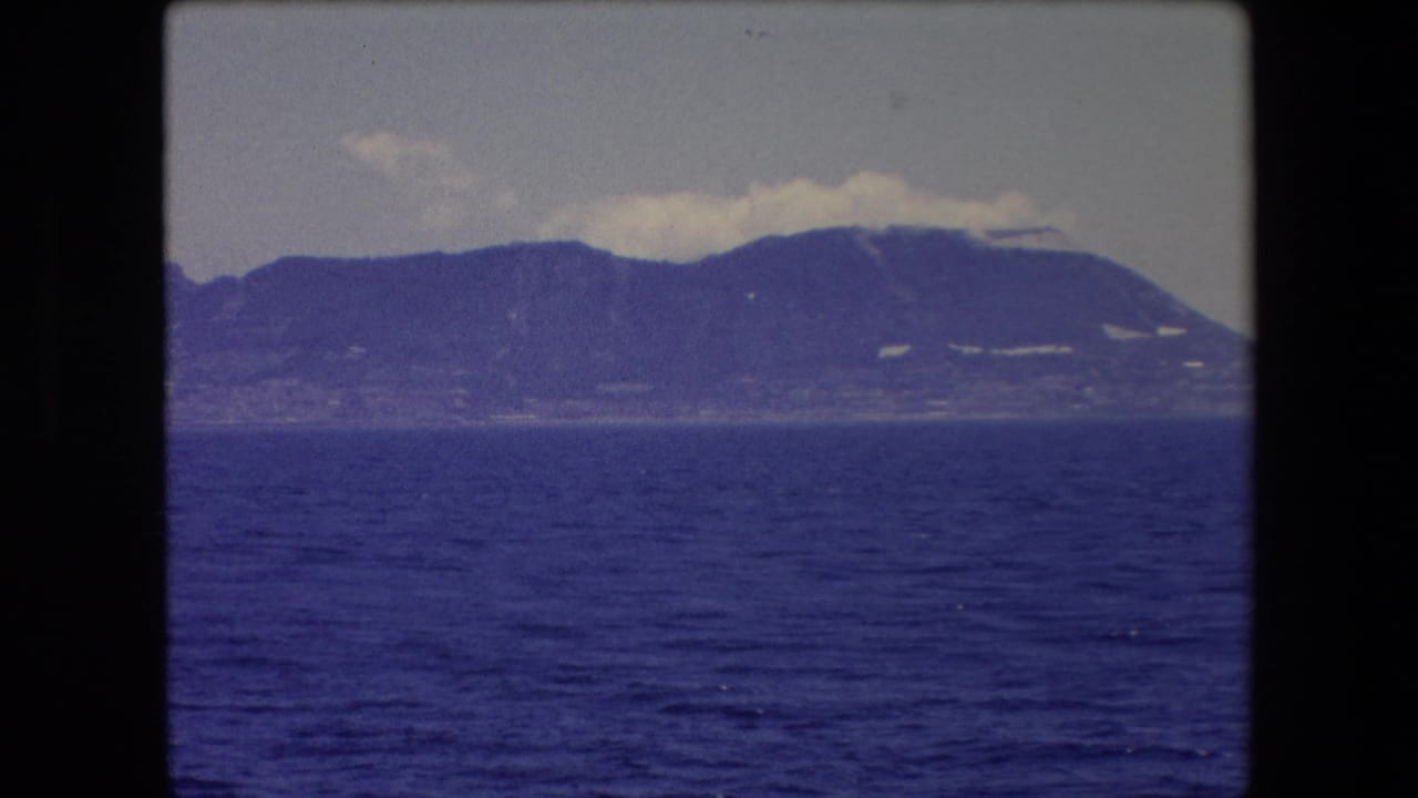 Blue sea and distant mountain coastline under a pale sky within the film frame.