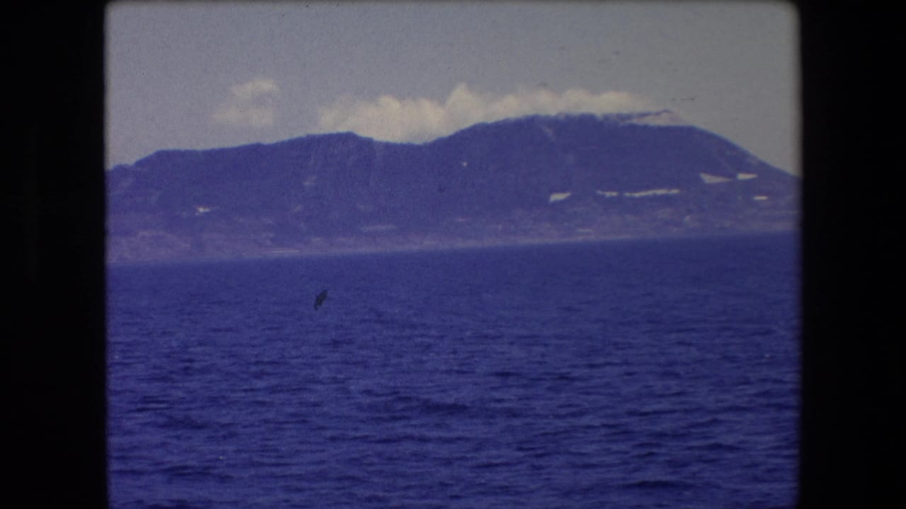 Rounded mountain ridge beyond blue sea with a small dark speck near the center.
