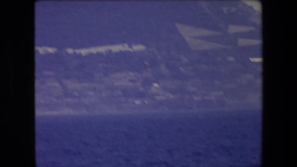 Soft 8mm frame of a hazy coastal slope and dark blue sea, likely filmed from a boat near Barcelona according to the clip metadata.