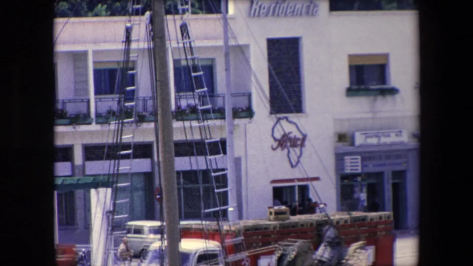 1971 Barcelona waterfront view of the Residencia Africa building area, with boat masts and ladders crossing the foreground and older cars parked near the facade.