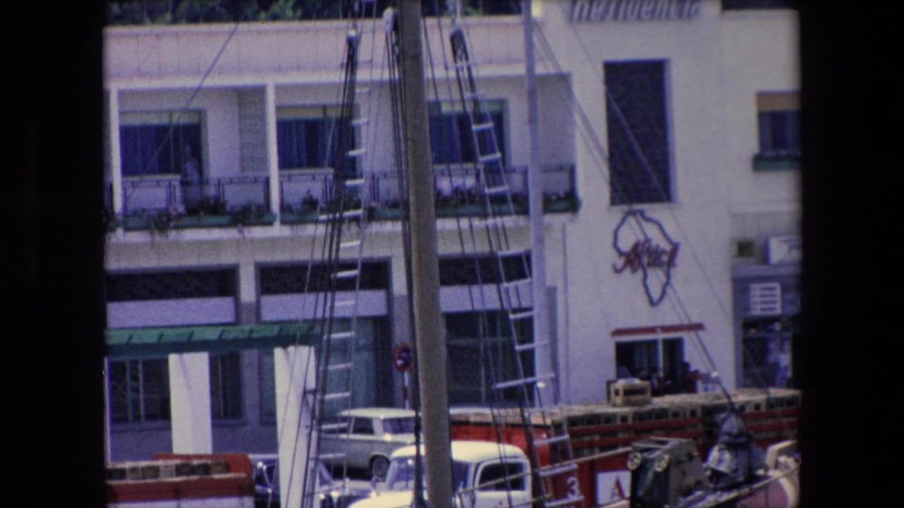 1971 Barcelona dockside view with the Residencia Africa sign partly visible above a facade, a painted Africa outline, rigging, ladders, and a small parked car below.