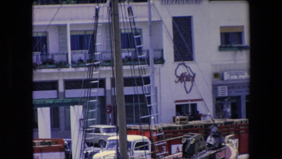 1971 Barcelona waterfront street scene with boat masts and ladders in the foreground, a white period car below, and the Residencia Africa facade behind them.