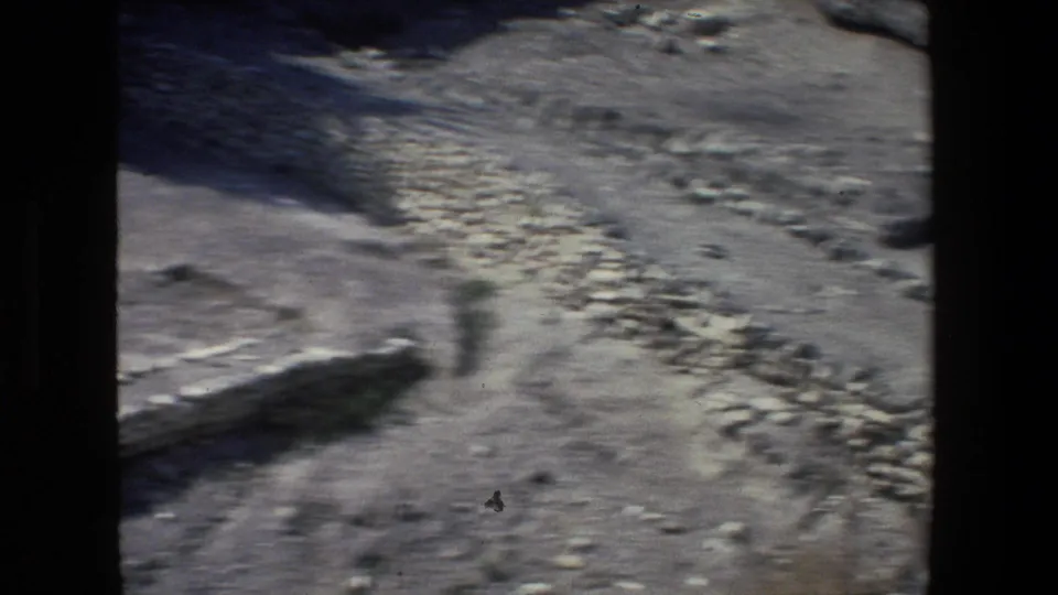 1972 Israel 8mm travel frame with motion blur across dry rocky ground, low stone alignments, scattered boulders, and canyon shadows.