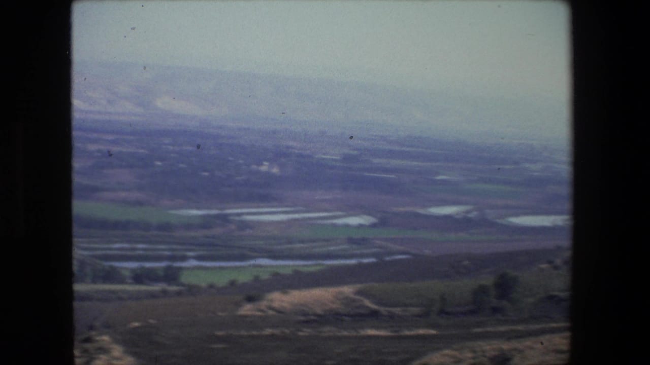 1972 8mm aerial-style view near Tel Aviv showing agricultural fields, small water ponds, open land, and distant pale hills under haze.