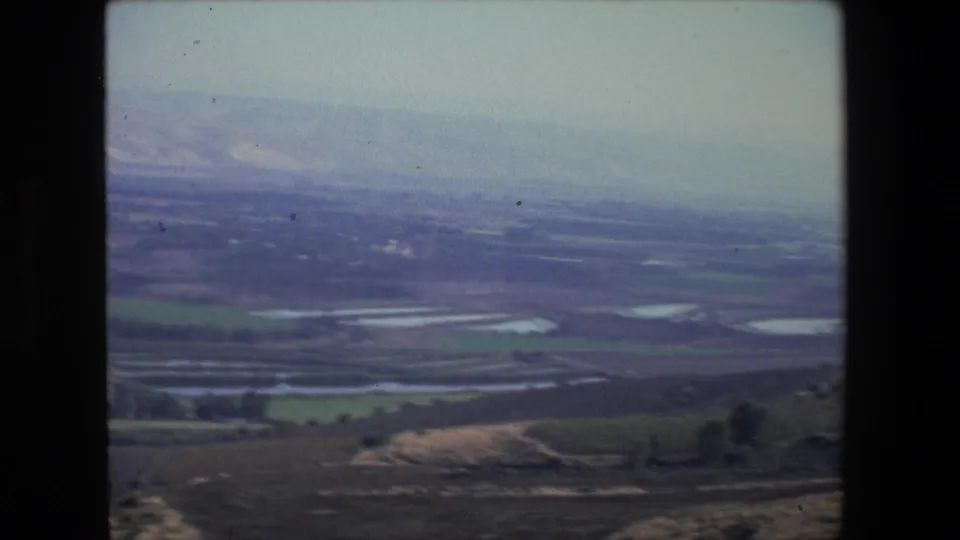 1972 8mm aerial-style view near Tel Aviv showing agricultural fields, small water ponds, open land, and distant pale hills under haze.