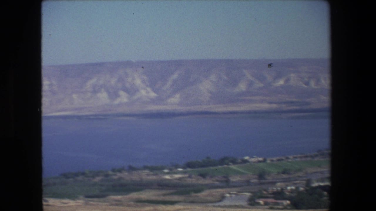 Blue water and pale hills seen from an elevated landscape viewpoint with black film borders.
