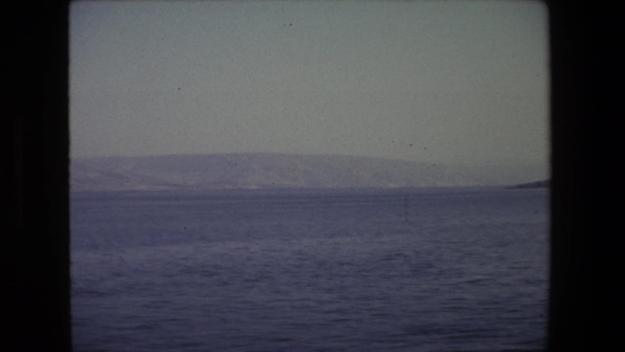 1972 Tel Aviv 8mm frame showing a subdued sea surface, distant low hills, hazy horizon, and dark projector or gate borders.