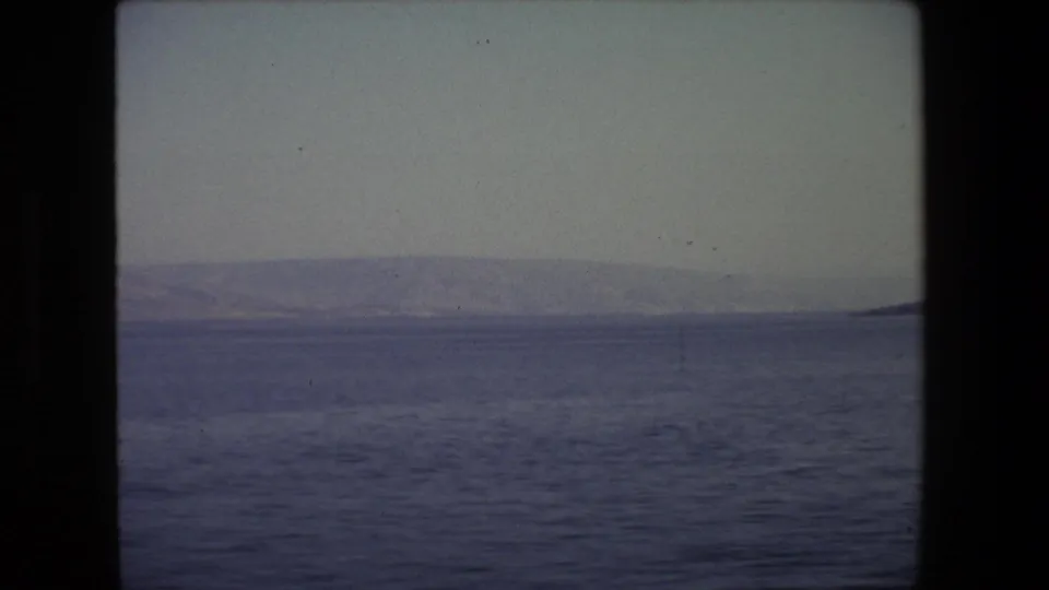 1972 Tel Aviv 8mm frame showing a subdued sea surface, distant low hills, hazy horizon, and dark projector or gate borders.