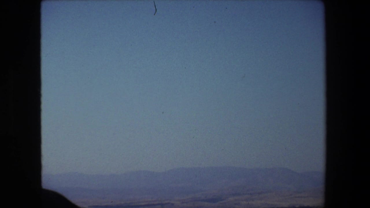 1972 Tel Aviv, Israel 8mm home-movie frame showing a soft blue sky, distant hills or shoreline, calm water, and dark film-frame borders.