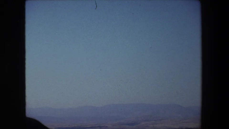1972 Tel Aviv, Israel 8mm home-movie frame showing a soft blue sky, distant hills or shoreline, calm water, and dark film-frame borders.