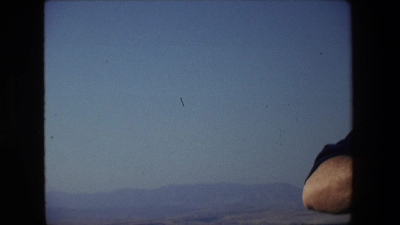 1972 Tel Aviv, Israel boat-view frame with hazy distant hills, calm water, blue sky, and a man's elbow briefly entering at the right edge.