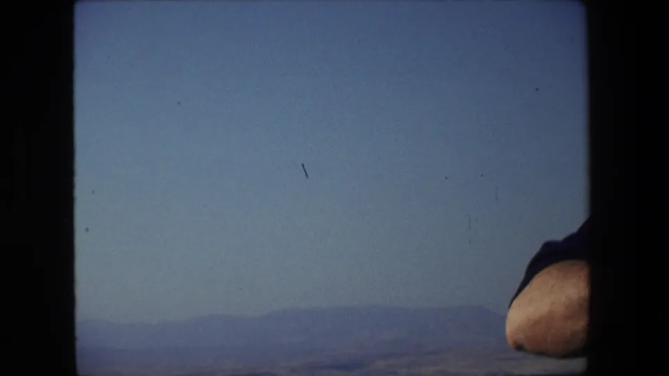 1972 Tel Aviv, Israel boat-view frame with hazy distant hills, calm water, blue sky, and a man's elbow briefly entering at the right edge.