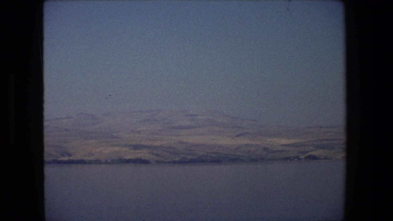1972 Tel Aviv, Israel home-movie frame showing calm water, a distant shoreline, low hills, and a lightly hazy blue sky.