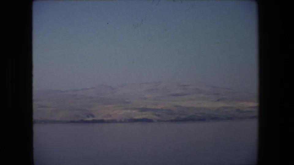 1972 Tel Aviv, Israel 8mm frame showing a wide view across calm water toward low dry hills under a pale hazy sky.
