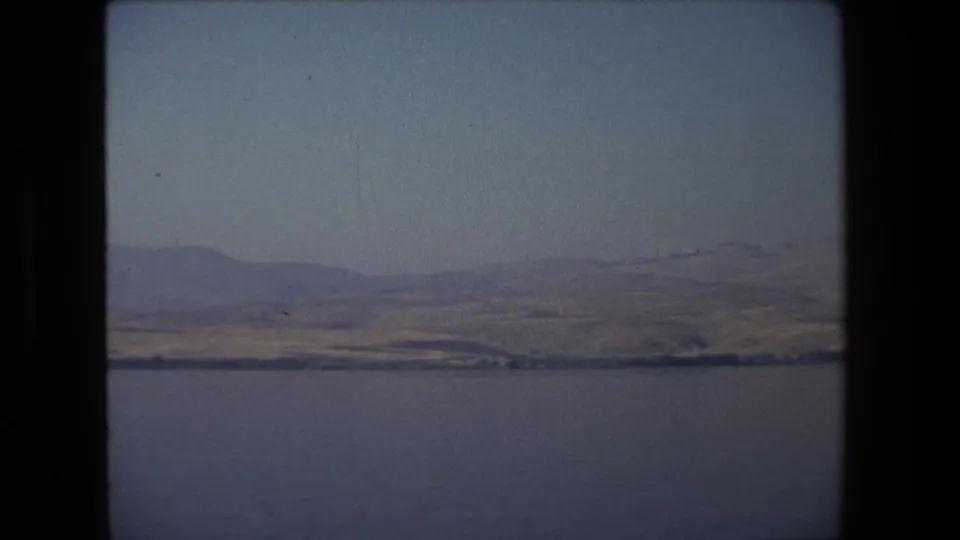 1972 Tel Aviv, Israel home-movie frame with a broad water surface, low rolling hills, and a faint shoreline beneath a hazy sky.