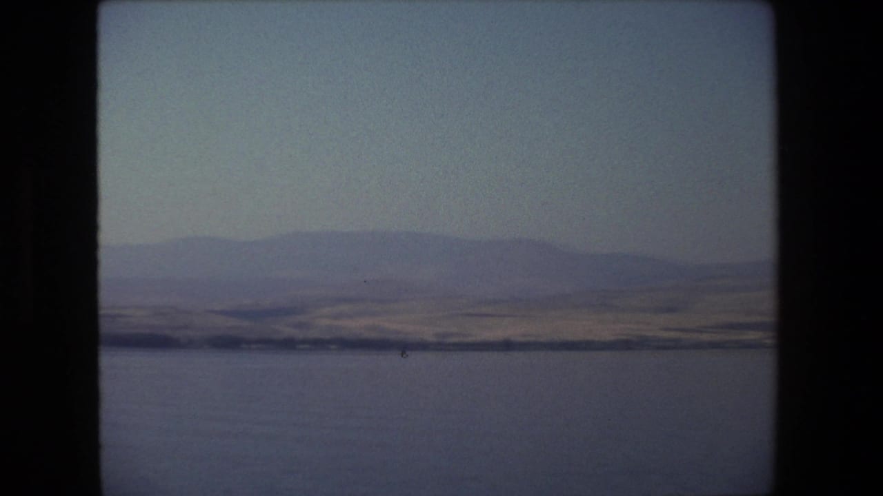 1972 Tel Aviv, Israel 8mm frame showing calm water in the foreground and muted hills beyond a thin shoreline.
