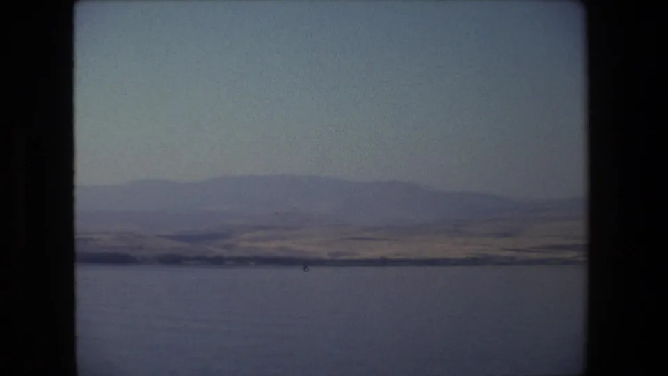 1972 Tel Aviv, Israel 8mm frame showing calm water in the foreground and muted hills beyond a thin shoreline.