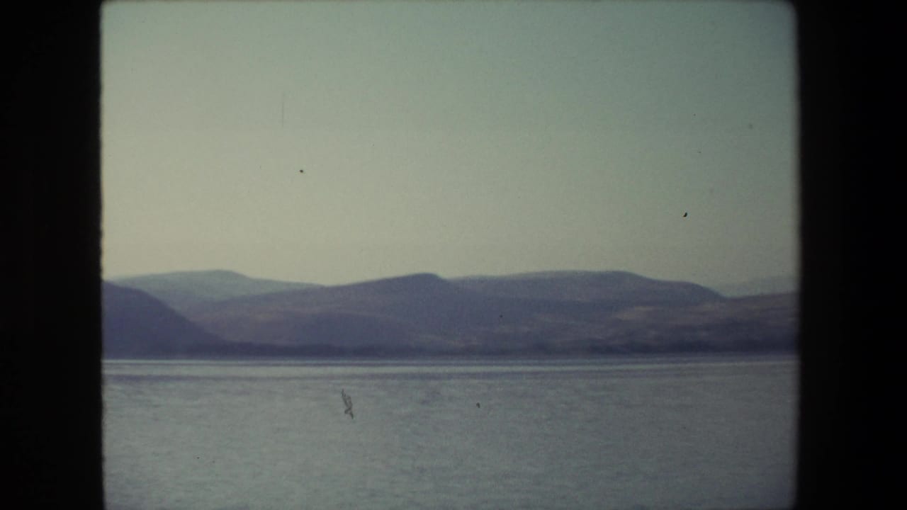 1972 Israel 8mm frame with a broad lake or coastal water view, low hills in the distance, and soft handheld home-movie exposure.