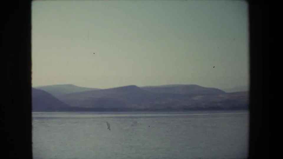 1972 Israel 8mm frame with a broad lake or coastal water view, low hills in the distance, and soft handheld home-movie exposure.