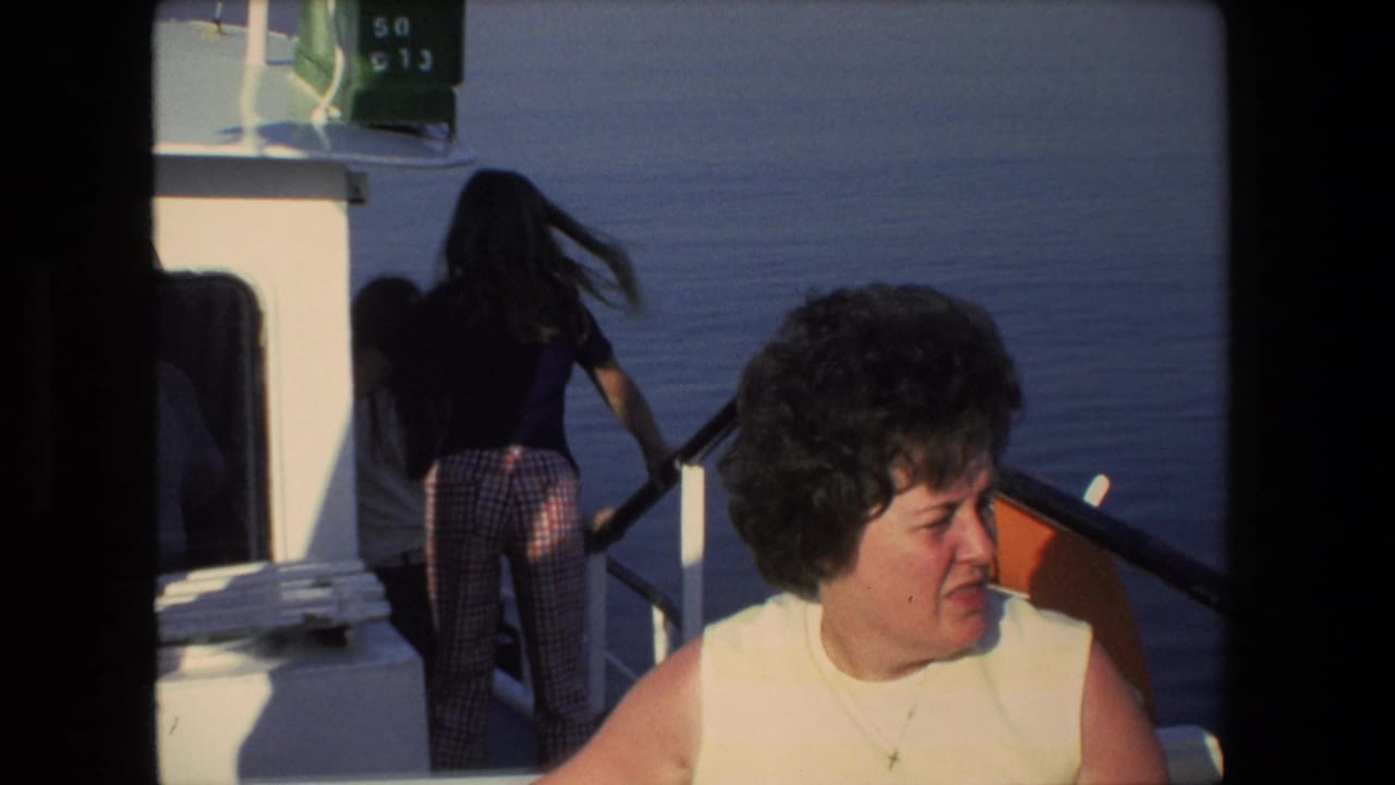 1972 Israel 8mm frame showing a woman in a white sleeveless top seated on a boat, with another long-haired passenger standing near the railing against open water.