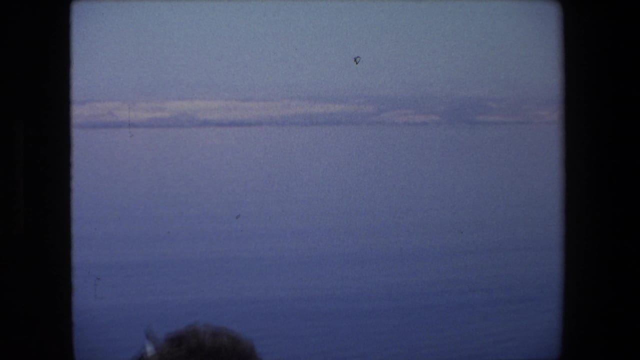 Blue sea and distant pale mountains seen from a boat, with a partial head at the lower edge.