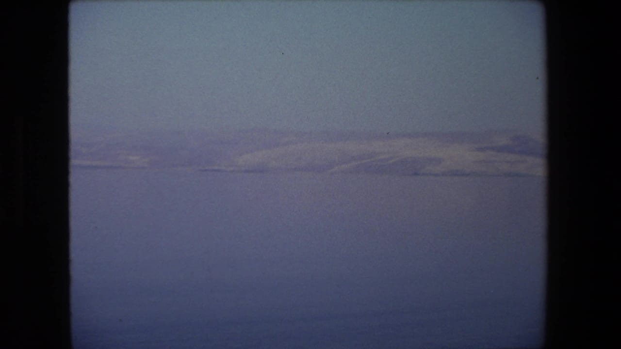 A quiet 1972 Tel Aviv travel view of blue water and distant pale mountains or shoreline under a clear sky, captured in soft 8mm color.