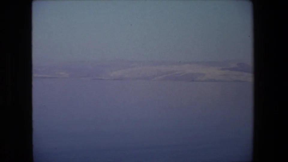 A quiet 1972 Tel Aviv travel view of blue water and distant pale mountains or shoreline under a clear sky, captured in soft 8mm color.