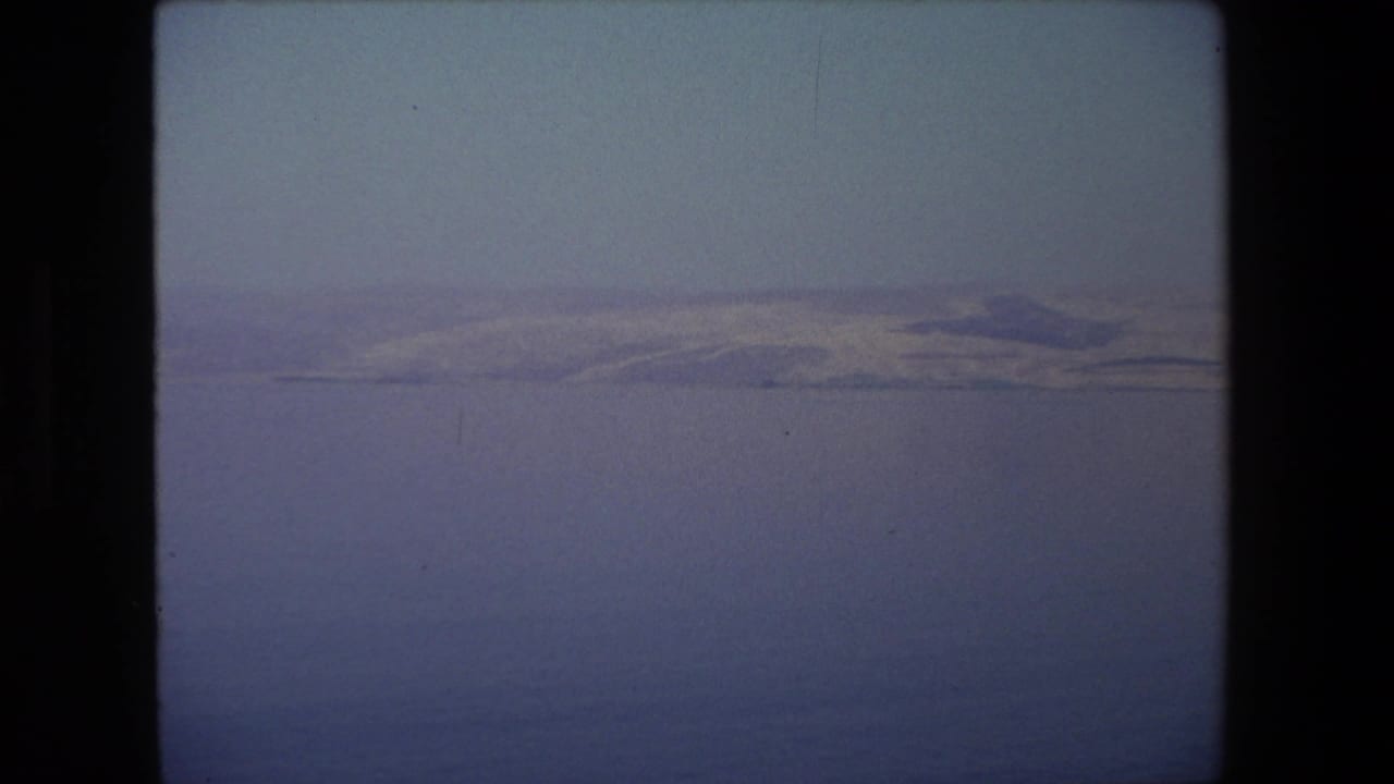 Calm blue water with distant hazy hills under a pale sky.