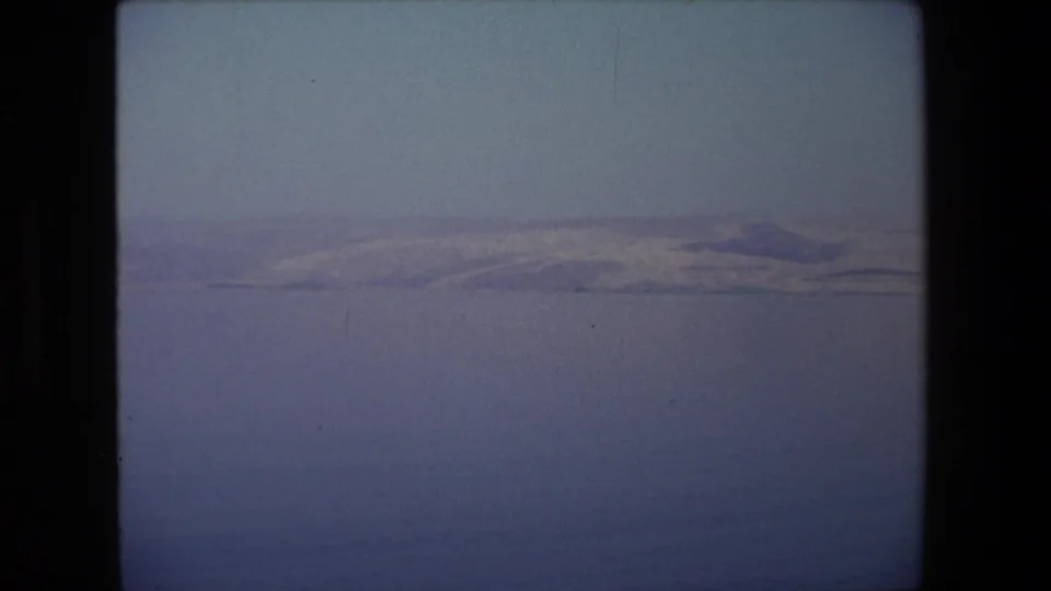 1972 8mm home-movie frame associated with Tel Aviv, Israel, showing calm water and a distant low mountain ridge beneath a hazy sky.