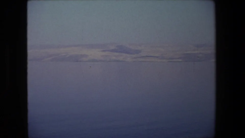 Vintage 8mm frame from the 1972 Israel footage showing a broad water surface and muted hills along the far horizon, with visible gate edges and grain.