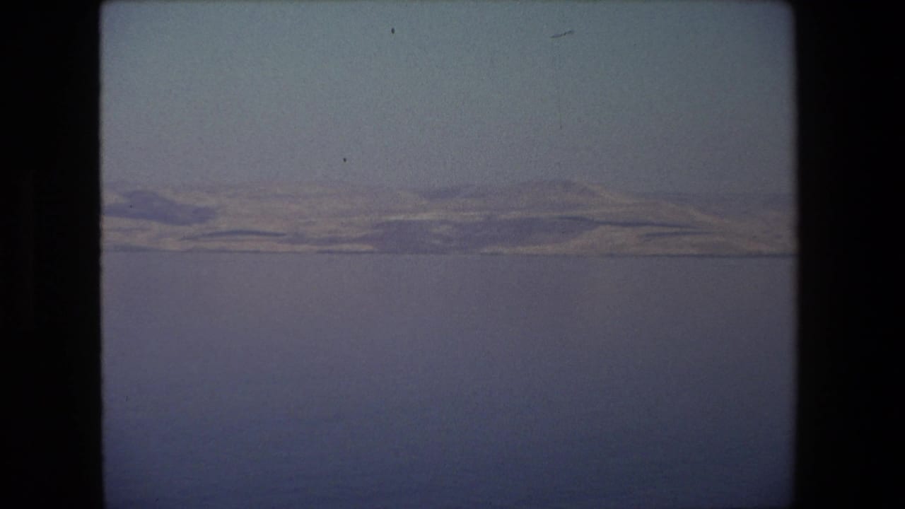 End frame of the 1972 8mm Israel landscape clip, showing a quiet water view with distant hills softened by haze and film grain.