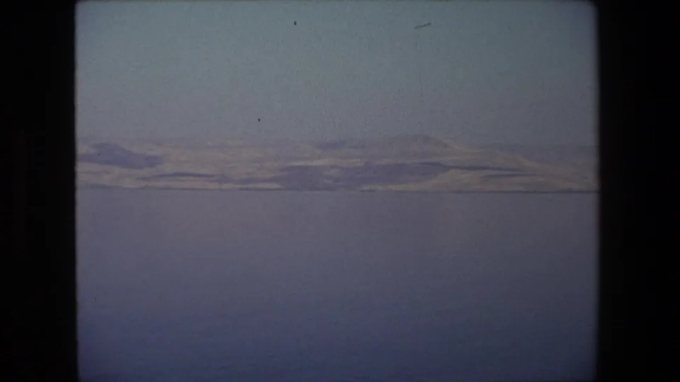End frame of the 1972 8mm Israel landscape clip, showing a quiet water view with distant hills softened by haze and film grain.
