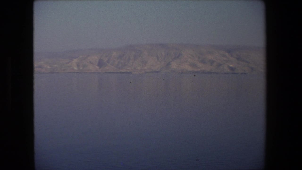 1972 8mm frame from Tel Aviv, Israel, with a broad arid ridge and low shoreline viewed across open water through soft home-movie color.
