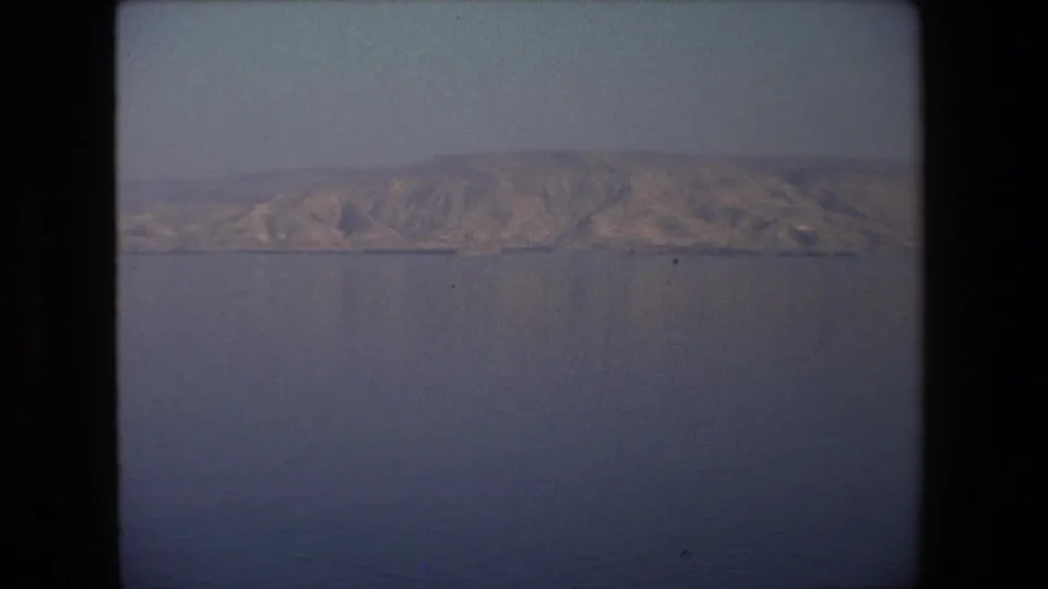 1972 8mm frame from Tel Aviv, Israel, with a broad arid ridge and low shoreline viewed across open water through soft home-movie color.