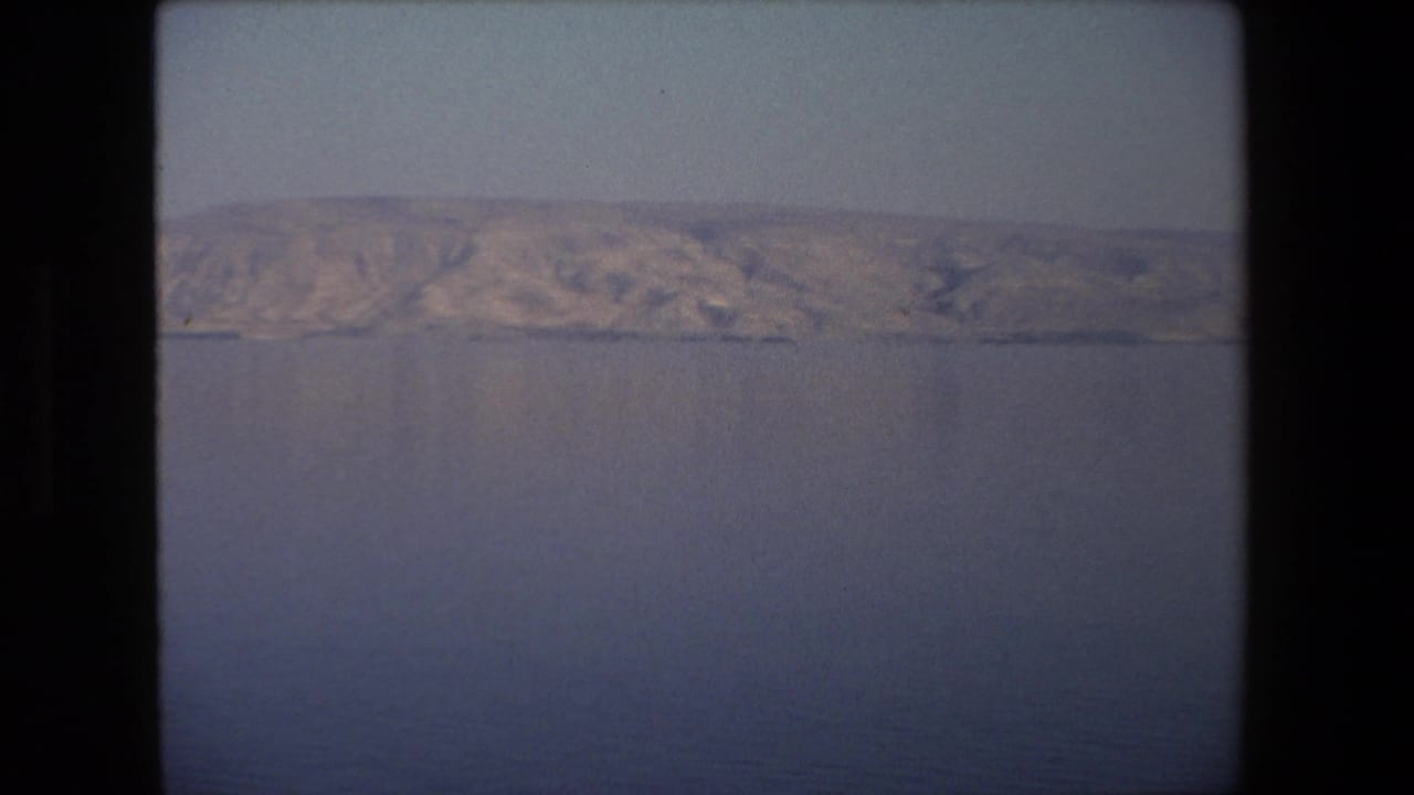 Wide water surface with low rugged hills in the distance and a pale sky.