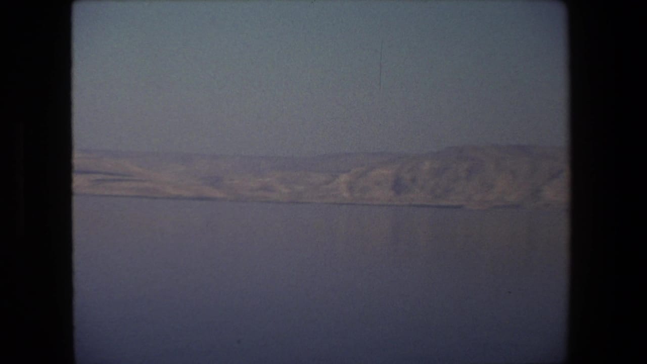 1972 Tel Aviv-area 8mm frame showing still water and a distant pale shoreline under a muted sky, with no people or buildings visible.