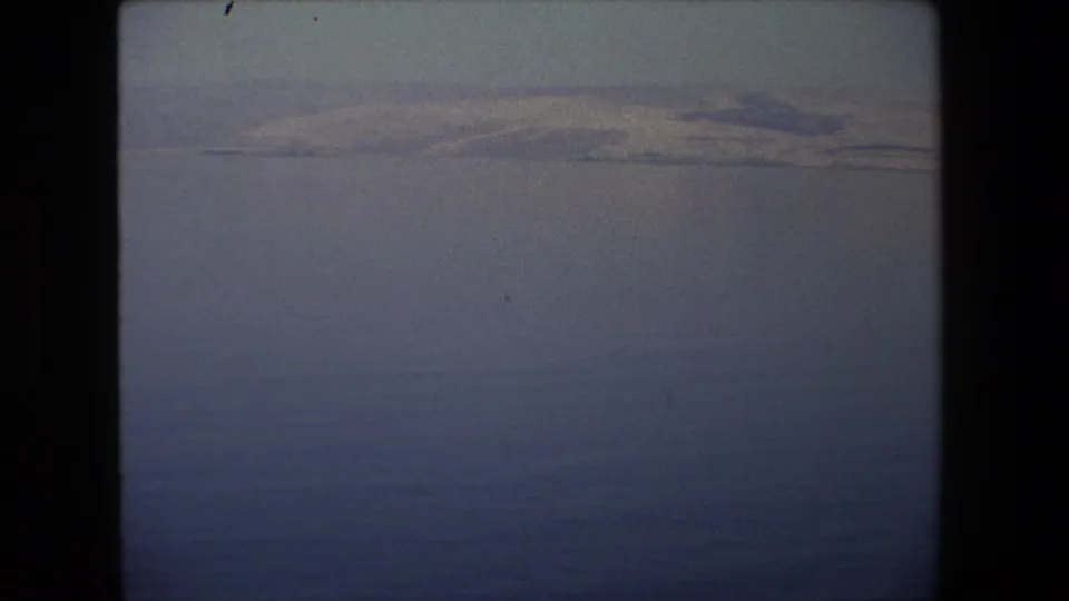 1972 Tel Aviv-area 8mm frame looking over dark blue water toward a low, pale shoreline with faint hills and visible home-movie grain.