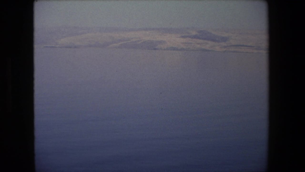 1972 Tel Aviv-area 8mm frame showing calm water in the foreground and a distant low bank under a pale, hazy sky.