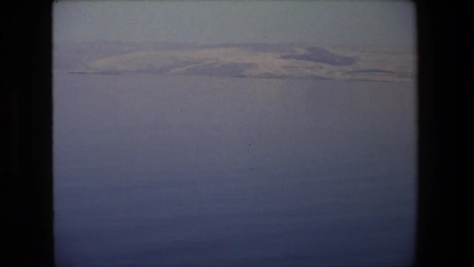 1972 Tel Aviv-area 8mm frame showing calm water in the foreground and a distant low bank under a pale, hazy sky.