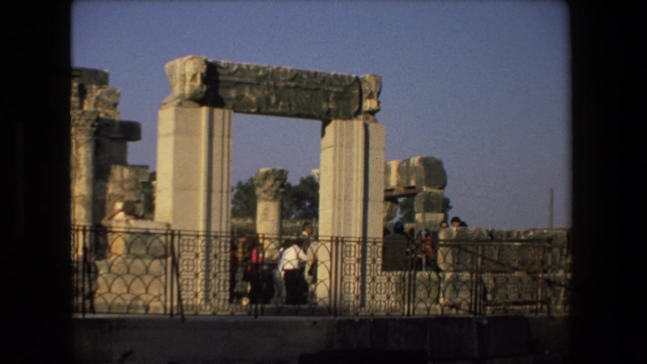Tourists gather beside tall weathered columns and a broken stone arch at an ancient ruin site in 1972 Israel travel footage.